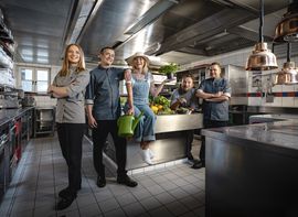 Ein motiviertes Küchenteam mit Köchen und Gärtnerin präsentiert sich in einer modernen Hotelküche
