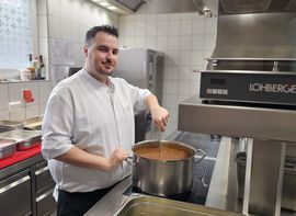 Koch rührt in Suppentopf in professioneller Hotelküche