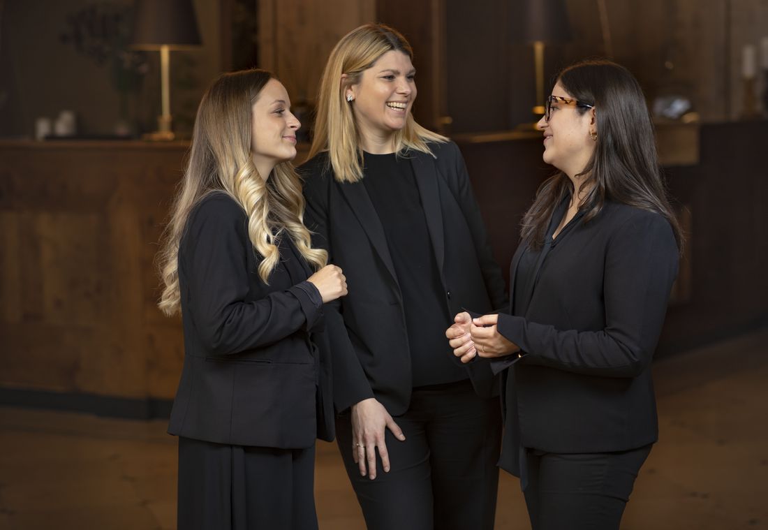 Drei Mitarbeiterinnen in Schwarz lachen beim Gespräch im Hotel