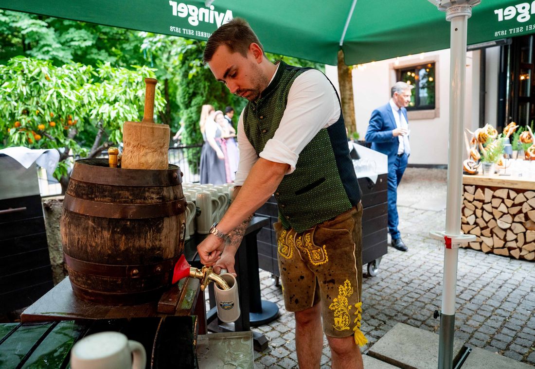 Mann in Tracht zapft Bier aus Holzfass beim Sommerfest