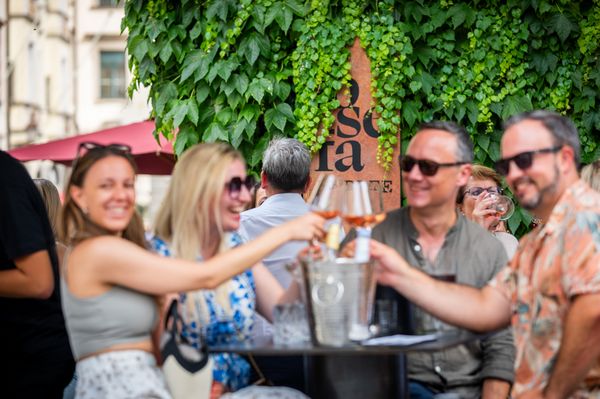 Eine Gruppe lächelnder Freunde, die draußen vor einer üppig mit Efeu bewachsenen Wand mit Roséwein anstoßen