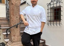 Koch in weißer Uniform steht lächelnd auf Treppe vor dem Gebäude