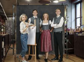 Vier Auszubildende der Platzl Hotels stehen nebeneinander und lachen in die Kamera. Darunter eine Auszubildende in bayerischer Tracht, zwei weitere in Platzl Hotel-Uniform und eine weitere Auszubildende in Jeans und weißem Hemd mit Malutensilien.